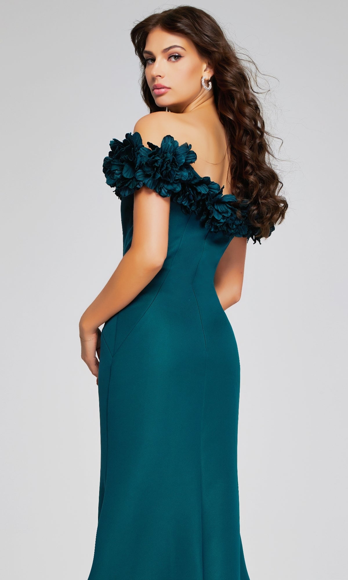 A woman with long brown hair models the Jovani 40595—a teal off-the-shoulder long formal dress with floral neckline detail—against a plain light background.